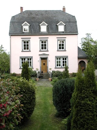 Rosafarbenes Herrenhaus mit grauem Dach, symmetrischen Fenstern und gepflegtem Garten., &copy; Conny Meier