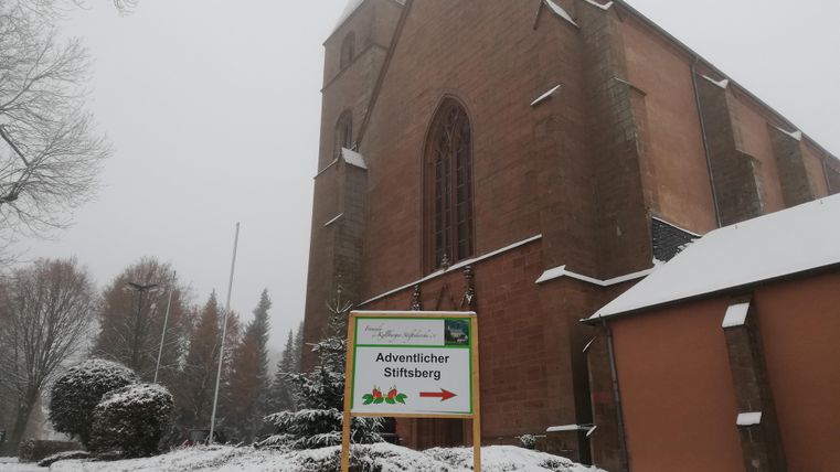 Une église dans la neige avec un panneau indiquant le Mont Stiftsberg de l'Avent. Le paysage est hivernal et invite à la visite.