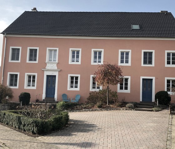 Une vieille ferme &agrave; la fa&ccedil;ade rose et aux portes bleues &agrave; Oberweis. Devant, il y a deux chaises bleues et un petit arbre dans le jardin de devant., &copy; TI Bitburger Land - Steffi Wagner