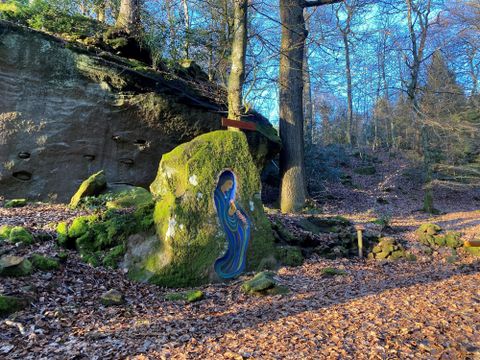 Une roche colorée avec une représentation artistique dans une forêt. Entourée de feuillage et de grands arbres sous la lumière du soleil.