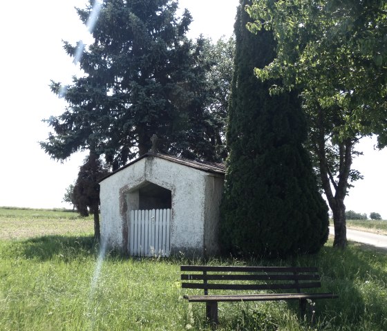 Petite chapelle &agrave; c&ocirc;t&eacute; d'un banc, entour&eacute;e d'arbres et d'une prairie, sur un chemin de terre., &copy; TI Bitburger Land
