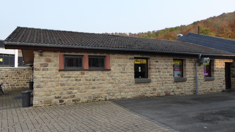 Een klein stenen huis met een donker dak. Het staat in een rustige omgeving, omringd door natuur.