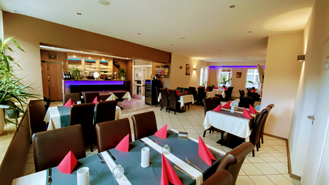 An inviting restaurant with elegant decor. The tables are set with white tablecloths and red napkins.