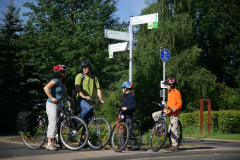 Un groupe de cyclistes se tient devant un panneau de signalisation. Ils portent des casques et se préparent à poursuivre leur chemin.