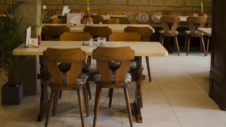 A cozy restaurant with wooden tables and chairs. In the background, additional seating and a relaxed atmosphere can be seen.
