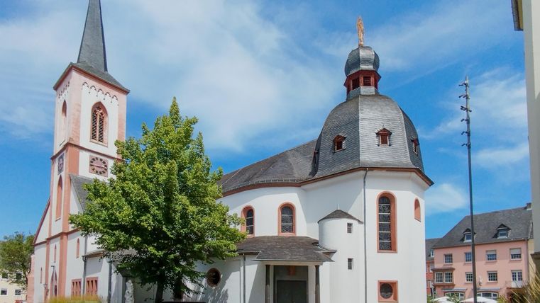 Een mooie kerk met een hoge toren en een markante koepel. Omgeven door bomen en een heldere lucht.