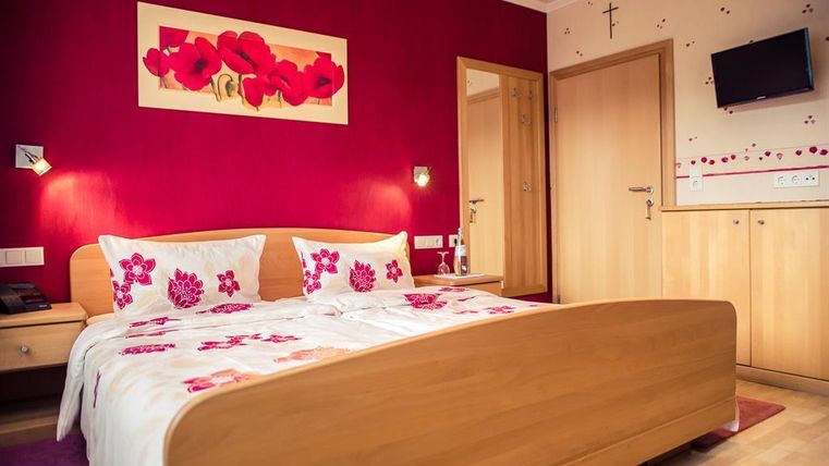 A cozy bedroom with a large bed and blooming decorations. The walls are painted red and there is a flat-screen TV.