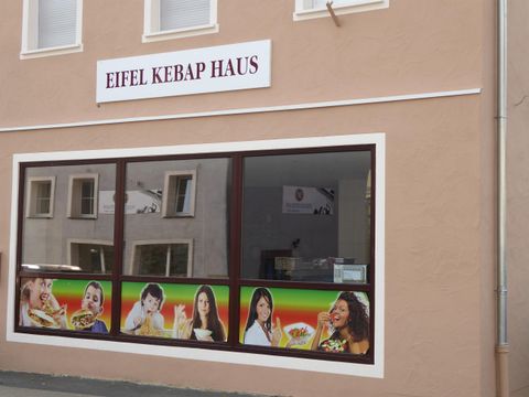 A restaurant named "Eifel Kebap Haus" with large windows. The facade displays images of various dishes and happy people.