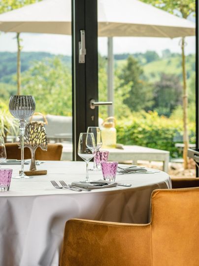 An elegant table with glasses and decorative elements stands in a restaurant. Through the windows, you can see a green landscape and umbrellas outside.