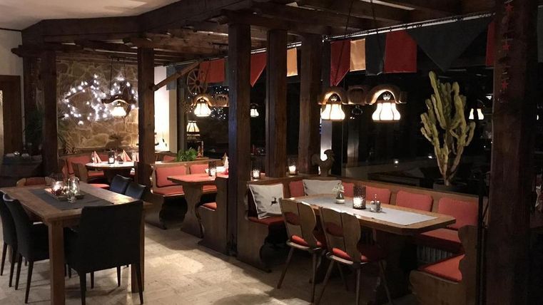A cozy restaurant with wooden tables and stylish lamps. The seating area offers an inviting atmosphere with soft cushions and plants.