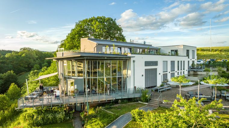 A modern building with large windows stands in a green environment. The terrace is perfect for relaxed hours outdoors.