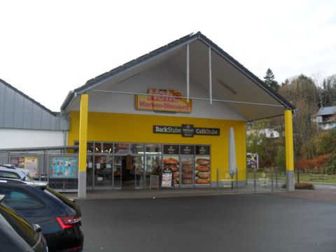 Un magasin de hard discount avec une façade jaune et une grande entrée. Devant le bâtiment, des voitures sont garées.