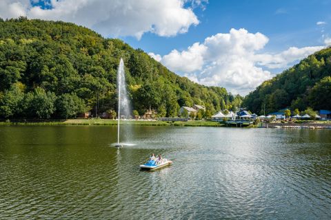 Ein malerischer See mit einem Wasserfall und grünen Hügeln im Hintergrund. Einige Menschen genießen eine Bootsfahrt auf dem ruhigen Wasser.