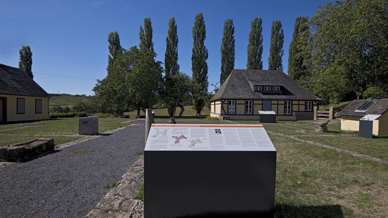 A historical site with several buildings and steles outdoors. In the background, tall trees stand under a clear blue sky.