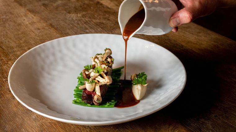 A beautifully arranged plate with vegetables and sauce. A hand pours the sauce over the dish.