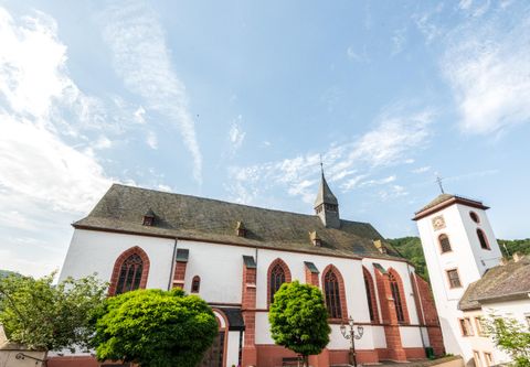 Eine historische Kirche mit roten und weißen Wänden unter einem klaren Himmel. Die Umgebung ist grün mit Bäumen und etwas Landschaft.
