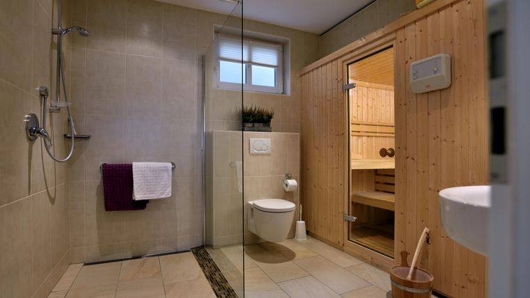 A modern bathroom with a shower, a sauna, and a sink. The walls are brightly tiled and the room design is contemporary.