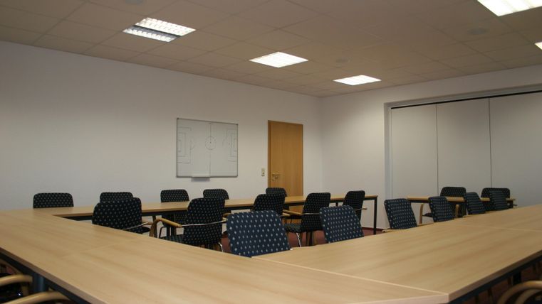 A modern conference room with long tables and chairs. The walls are bright and the room is well lit.