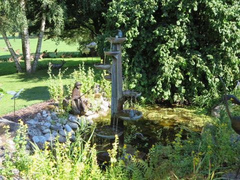 A beautiful garden with a small pond and a water column. Lush plants and a calm atmosphere invite you to relax.