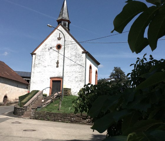 Kleine Kapelle mit spitzem Turm und orange umrahmten Fenstern in Etteldorf, umgeben von B&auml;umen und blauem Himmel., &copy; Tourist-Info Bitburger Land M.Mayer