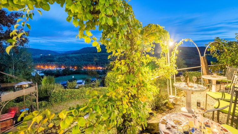 Une belle vue sur la terrasse des roses avec des vignes et une ambiance lumineuse du soir. Des tables sont préparées pour les invités en plein air.