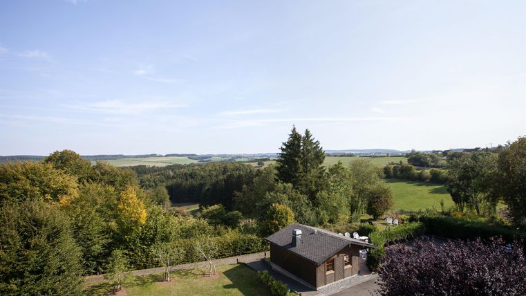 A picturesque landscape with gentle hills and lush green. In the foreground, there is a small house under a blue sky.