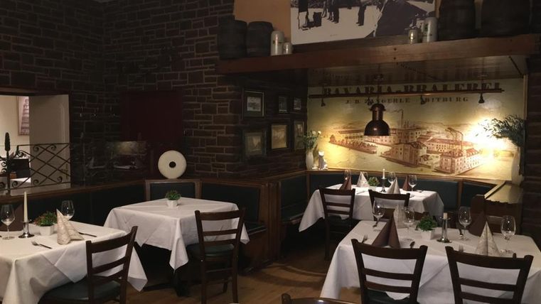 A cozy restaurant with elegantly set tables. The walls are adorned with brick and decorative pictures.