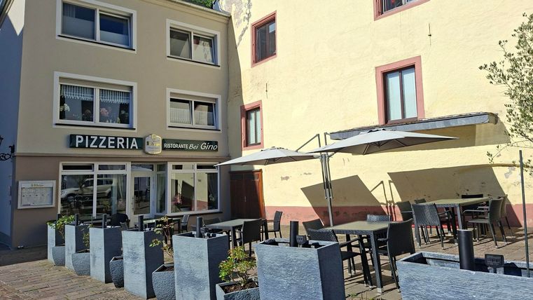 Een pizzeria met buitenruimte in een charmante straat. Tafels en stoelen zijn onder parasols geplaatst.