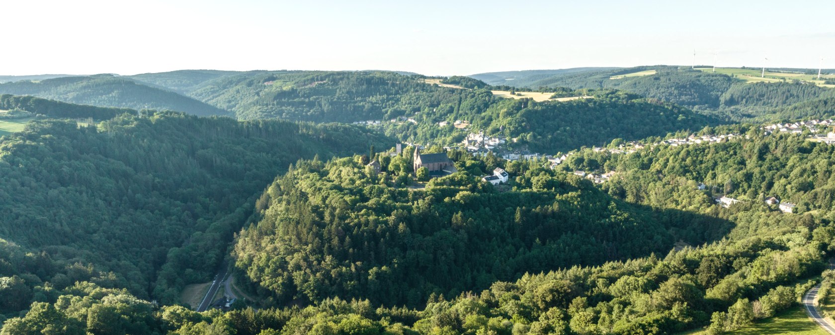 Luchtfoto van een groen heuvellandschap met een dorp op een heuvel omringd door bossen en velden onder een heldere hemel., &copy; Eifel Tourismus GmbH, Dominik Ketz