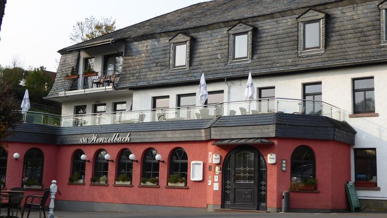 Een charmant hotel met een rode gevel en een balkon. De omgeving lijkt uitnodigend en goed onderhouden.