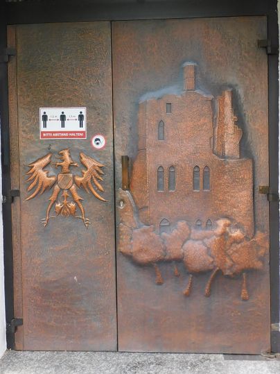 An artistically designed door with relief-like motifs of buildings and animals. There is also a sign with symbols for the restrooms.
