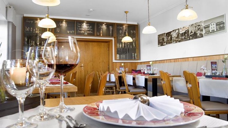 A cozy restaurant with elegant tablecloths and festively laid tables. In the background, there are pictures on the wall and warm light from lamps.