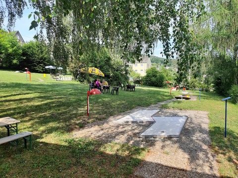 Ein ruhiger Garten mit Sitzgelegenheiten und einem wunderschönen, grünen Rasen. Es gibt einige Schirme und Spielbereiche für Aktivitäten.