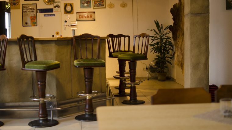 A cozy bar with several stools and a rustic interior design. Decorative signs and plants are visible in the background.