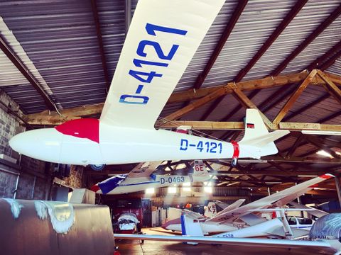 A glider is hanging in a hall. It is white with a red nose and bears the registration D-4121.