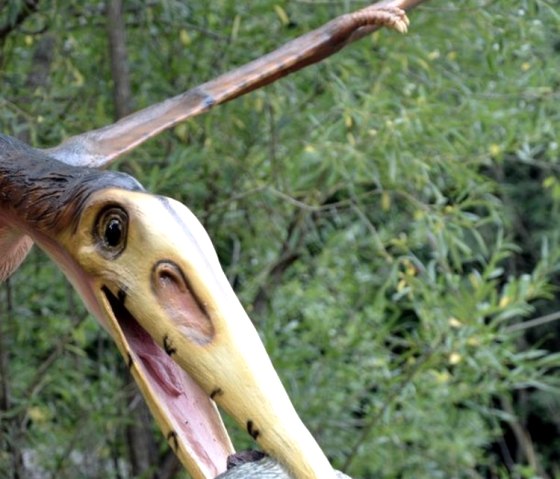 Un mod&egrave;le de dinosaure volant tient un poisson dans son bec, entour&eacute; de v&eacute;g&eacute;tation verte dans le Dinopark.