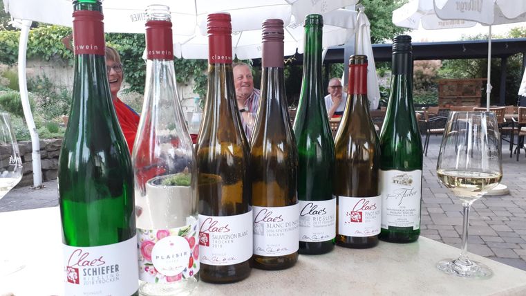 Une rangée de bouteilles de vin est posée sur une table, certaines avec un bouchon rouge et d'autres avec un bouchon vert. À l'arrière-plan, des personnes floues et une ambiance chaleureuse.