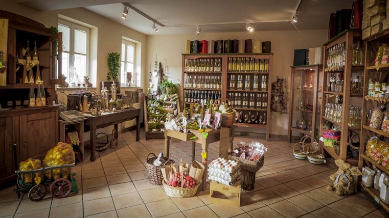 Een gezellige winkel met schappen vol voorraden en lekkernijen. In het midden staan manden en tafels met verschillende producten.