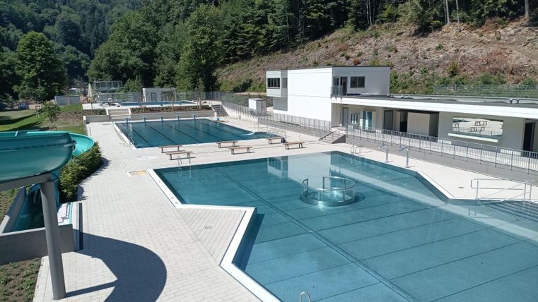 Une piscine moderne avec plusieurs bassins et une eau claire et bleue. L'établissement est entouré d'arbres et dispose de beaucoup d'espace pour se détendre.