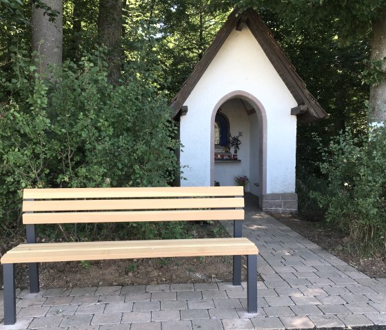 Kleine Kapelle am Waldrand mit einer Holzbank davor. Der Weg zur Kapelle ist gepflastert, umgeben von B&auml;umen und Str&auml;uchern., &copy; TI Bitburger Land