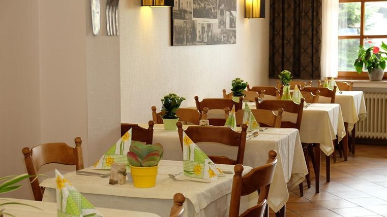 A cozy restaurant with simple, white tables and chairs. The tables are decorated with colorful napkins and small plants.