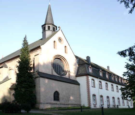 Das Kloster St. Thomas zeigt gotische Architektur mit einem Rosettenfenster und einem kleinen Turm, umgeben von B&auml;umen und einem klaren Himmel., &copy; TI Bitburger Land