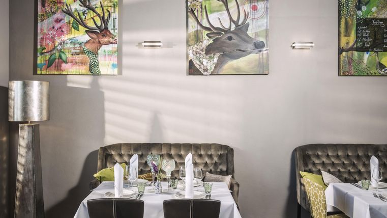 A stylish restaurant with elegant tables and cozy benches. The walls are decorated with colorful animal portraits.