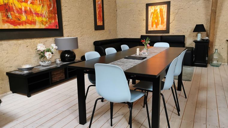 A modern dining area with a long table and blue chairs. Colorful paintings hang on the walls, and there is a pleasant atmosphere.