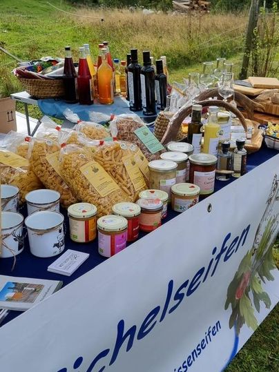 A colorful stand with various regional products, including jams, beverages, and pasta. In the background, meadows and mountains are visible.
