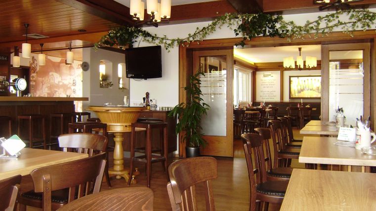 Un restaurant chaleureux avec des tables et des chaises en bois. Les murs clairs et les lumières au plafond créent une atmosphère accueillante.
