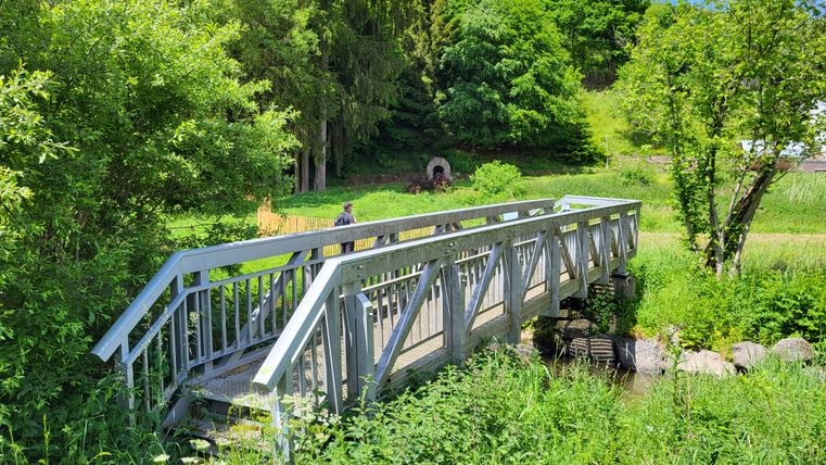 Eine kleine Holzbrücke über einen Bach in einer grünen Landschaft.