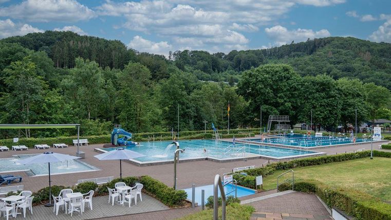 A beautiful outdoor pool with several basins and a green surrounding. In the background, there are trees and a blue sky.