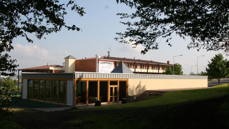 A modern building with large windows in a green environment. The sky is clear and the atmosphere is calm.