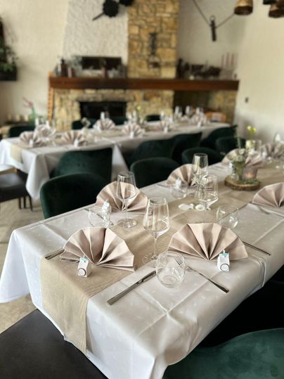 An elegantly set table with white tablecloths and decorative napkins. In the background, a rustic fireplace is visible, creating a cozy atmosphere.